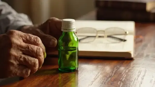 A man's hands turning a small green bottle a quarter turn on a desk to read its back